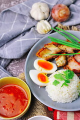 Thai dish '' Khao mu daeng '' or red sauce pork stew with rice and spring onions served in a gray plate on the black table in the restuarant