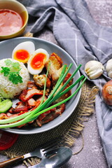 Thai dish '' Khao mu daeng '' or red sauce pork stew with rice and spring onions served in a gray plate on the black table in the restuarant