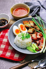 Thai dish '' Khao mu daeng '' or red sauce pork stew with rice and spring onions served in a gray plate on the black table in the restuarant
