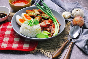Thai dish '' Khao mu daeng '' or red sauce pork stew with rice and spring onions served in a gray plate on the black table in the restuarant