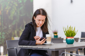 Portrait of young business woman use smartphone at cafe outdoors. Beautiful girl use online business call. Startup business caucasian woman, sme telemarketing job.Summer windy day.