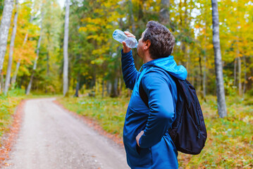Middle age man hiker with backpack drinking water from the bottle, having break in autumn forest.
