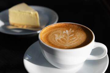 Latte art coffee in white cup whit cheese cake at back with dark background