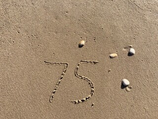 On the beach in the sand is carved the number 75