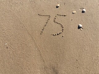 Fototapeta na wymiar On the beach in the sand is carved the number 75