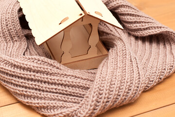 Figure of house and warm scarf on light background. Concept of heating season.
