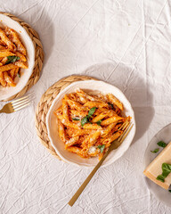 Italian cuisine penne pasta with tomato and pepper sauce on a table for two with a golden fork, hard shadows, minimal stylization, textured top view