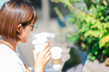 テラスでコーヒーを飲みながらパソコンを見る女性