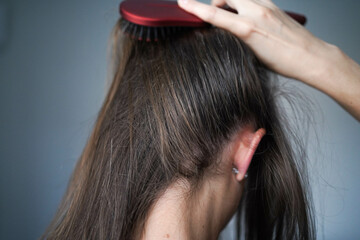 A woman combs her hair. Gray hairs on the head of a young girl. Long gray hair. The initial stage of gray hair. The problem of gray hair in women.