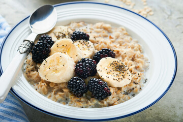 Oatmeal. Bowl of oatmeal porridge with blackberry, bananas and chia seeds on gray concrete old table background. Top view in flat lay style. Natural ingredients. Hot healthy breakfast and diet food.