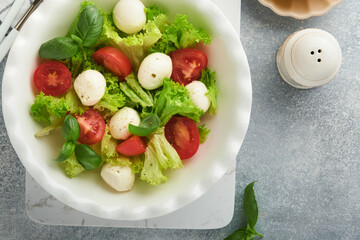 Caprese salad. Italian caprese salad with sliced tomatoes, mozzarella cheese, basil, olive oil in white plate over white background. Delicious Italian food. Top view. Rustic style.