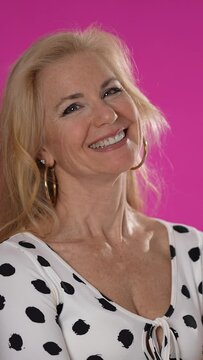 Vertical video close up of attractive mature woman entrepreneur looking to camera and smiling. Middle aged confident fashion woman standing and crossing hands. Portrait on pink background.