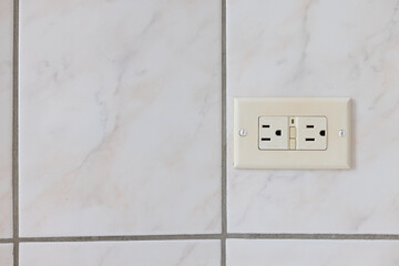 Electrical plug type B on the tiled wall in a bathroom.