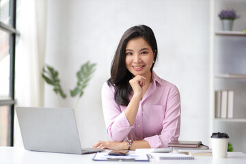 Portrait of a charming Asian business woman smiling happily working on a laptop in the home office.