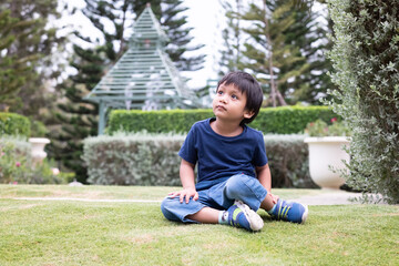 Adorable asian boy sitting alone in the garden and raise his head up to the sky looking at the beauty of nature.
