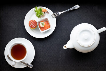 Afternoon hot tea in white cup with teapot, macaron, salmon and shrimp. Traditional drink with snacks. Top view.