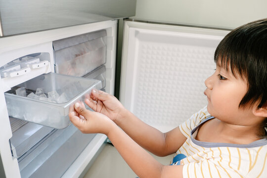 Little Asian kid making some ice using the ice maker in the refrigerator