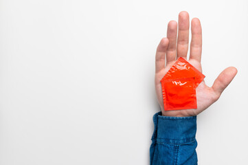 Male hand holding a condom in a red package on a white background