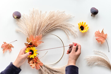 Hands making dried floral wreath from dry pampas grass and Autumn leaves. Hands tie decorations to...