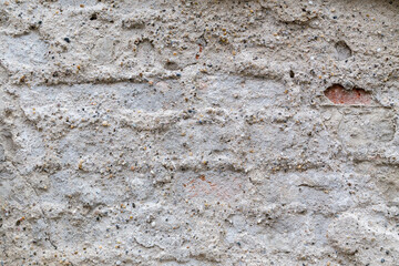 Obraz na płótnie Canvas Old brick wall with weathered, pebble dash plaster, roughly and thinly covering the bricks. The plaster is very uneven and missing in some places, revealing the red bricks behind. Abstract background.