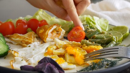 Breakfast of fried eggs and vegetables, cherry tomatoes are cut with a knife. Hearty and healthy breakfast with a balanced composition for proper nutrition. Keto diet high in fat and protein.