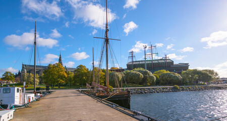 Fototapeta na wymiar Old wood sail ship at a pier in the bay Ladugårdsviken old gothic museum building and the Vasa museum a colorful sunny autumn day in Stockholm