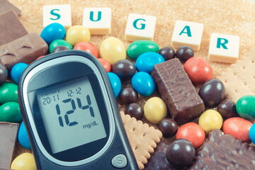 Glucometer with bad result sugar level and heap of sweets containing a lot of sugar. Reduction eating unhealthy food