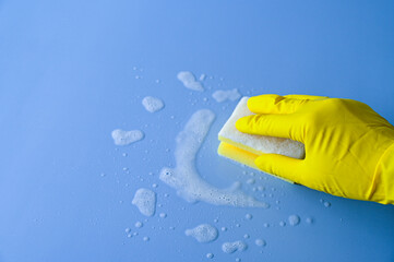 Hand with yellow rubber glove on holds a cleaning sponge on a blue background.