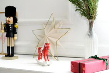 Christmas decor. A toy rocking horse, a nutcracker, a gift, a vase with Christmas tree branches stand on a white elegant shelf