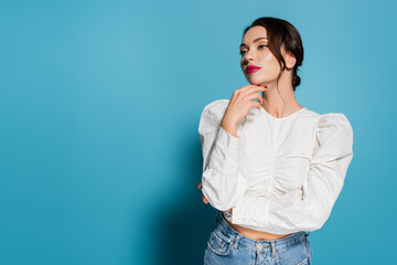 dreamy young woman in white blouse looking away isolated on blue.