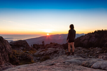 Adventurous Woman Hiker on top of Canadian Mountain Landscape. Sunny Sunset Sky. Top of Mt Seymour near Vancouver, British Columbia, Canada. Adventure Travel Concept