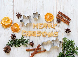 Christmas holiday background. festive decor, cookie cutters, cinnamon, nuts, cones, fir branches, Merry Christmas text of cookies on wooden table. top view