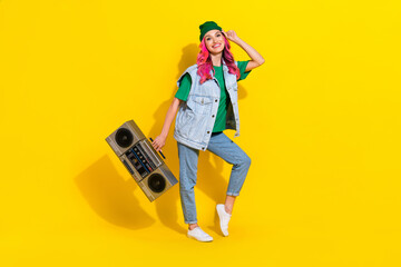 Full length photo of funny positive lady wear jeans waistcoat holding boombox smiling isolated yellow color background