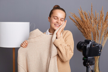 Portrait of satisfied delighted young adult woman blogger stylist with bun hairstyle shooting video...