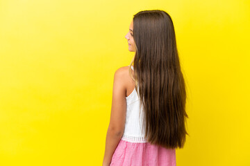 Little caucasian girl isolated on yellow background in back position and looking side