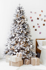 New Years bright interior bedroom with decorated Christmas tree with garlands, white bed, beige blanket, photos on the wall. Christmas interior. Scandinavian style. Location for photo shoot.