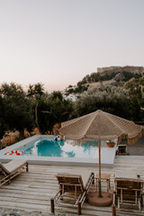 The relaxing scene of a swimming pool area, sun umbrella, trees and loungers at sunset in Rhodes Island, Greece