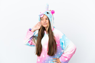 Little caucasian girl wearing unicorn pajama isolated on white background listening to something by putting hand on the ear