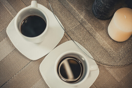 Two white cups of hot aromatic coffee on a brown table with candles. Composition in brown and beige tones. Background image for your creativity and design.