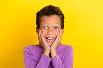 Photo of astonished schoolkid beaming smile arms touch cheekbones isolated on yellow color background