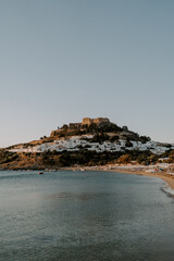 Fototapeta na wymiar The serene view of Lindos Beach and The Acropolis in Rhodes. Rocks, sand, beach, waves, sea, blue sky