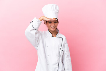 Little caucasian chef girl isolated on pink background looking far away with hand to look something