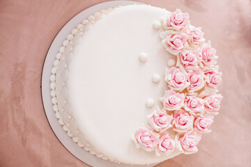 Gorgeous beige birthday cake with pink flowers on the table. Background image for your creativity and design.