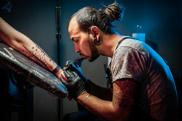 Portrait of man tattoo master with dreadlocks showing process of creation tattoo on female body...