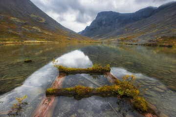 Rainy northern mountains and lake with a ruined pier in autumn