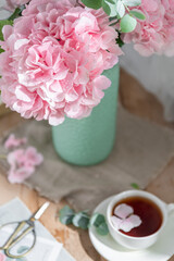 Composition with tea mug and beautiful pink flowers hydrangeas in vase