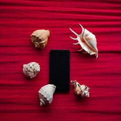 Creative minimalistic composition with a mobile phone and a seashell in light warm colors on a red textured background