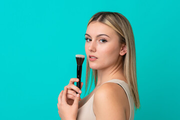Young caucasian woman isolated on blue background holding makeup brush