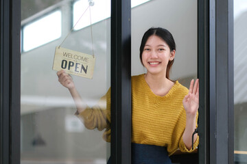 Young Asia manager girl changing a sign from closed to open sign on door cafe looking outside waiting for clients after lockdown. Owner small business, food and drink, business reopen again concept