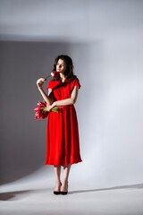 Full lengt image of a female model in red dress holding a bouquet of tulips and spins, isolated grey background.